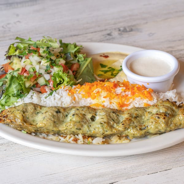 Baba Pita's Mediterranean chicken kebab with rice, salad, hummus, and white sauce on a white plate.