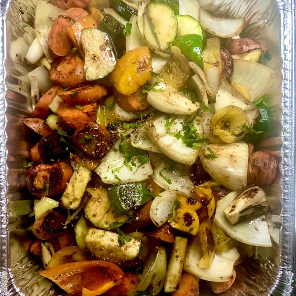 Close-up of roasted Mediterranean vegetables including carrots, zucchini, onions, and bell peppers in a foil pan.