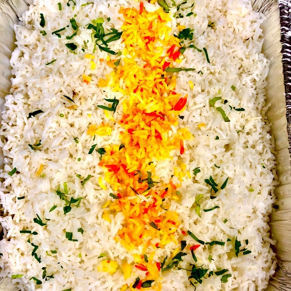 White rice with a vibrant yellow and red saffron stripe, garnished with green herbs in a foil pan.